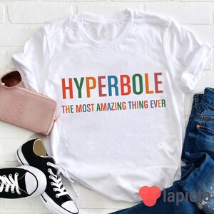 Pu&ograve; includere: Maglietta bianca con il testo "HYPERBOLE THE MOST AMAZING THING EVER" in colori arcobaleno.