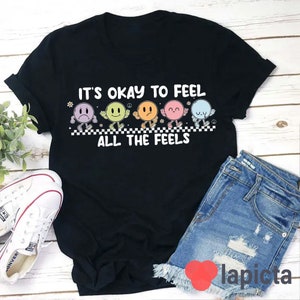 May include: Black t-shirt with the text "It's okay to feel all the feels" and a row of six colorful cartoon faces with different expressions.