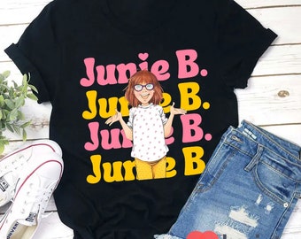 Op de afbeelding: Zwart T-shirt met een roze en gele afbeelding van Junie B. Jones, een personage uit de kinderboekenreeks. De afbeelding toont Junie B. Jones met haar kenmerkende bril en een roze jurk met witte stippen.