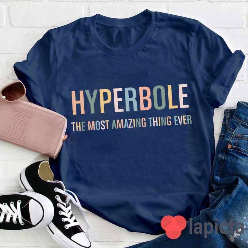 Pu&ograve; includere: Una maglietta blu navy con il testo "HYPERBOLE THE MOST AMAZING THING EVER" in colori arcobaleno.