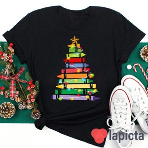 May include: Black t-shirt featuring a Christmas tree design made from colourful crayons. The tree is decorated with fairy lights.