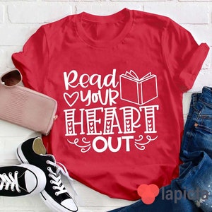 Puede incluir: Camiseta roja con texto blanco que dice "Read your heart out" con un gráfico de libro y corazones.