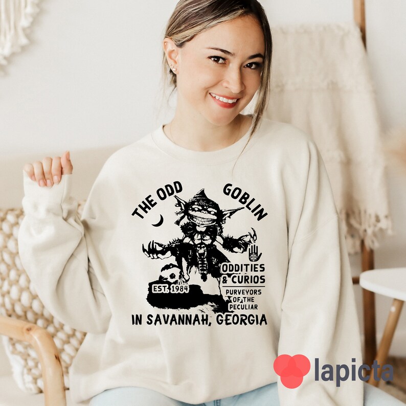 May include: A white sweatshirt with a black graphic of a goblin holding a sign that says "The Odd Goblin, Oddities & Curios, Est. 1984, Purveyors of the Peculiar, In Savannah, Georgia".