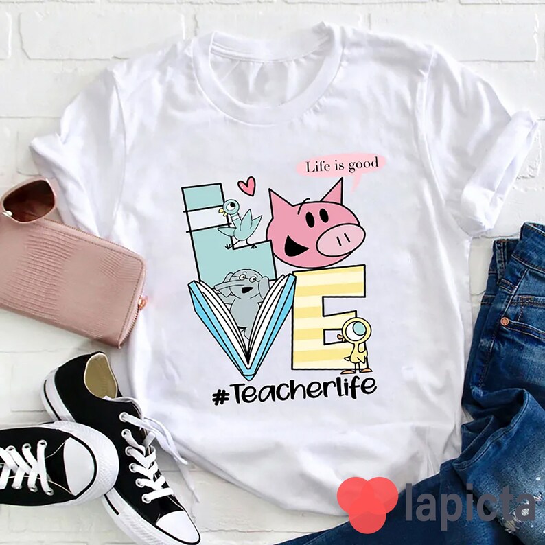 Op de afbeelding: Wit T-shirt met een afbeelding van het woord "LOVE" gemaakt van illustraties van een varken, een vogel, een boek en een eend. De tekst "Life is good" staat boven de afbeelding en de tekst "#Teacherlife" staat onder de afbeelding.