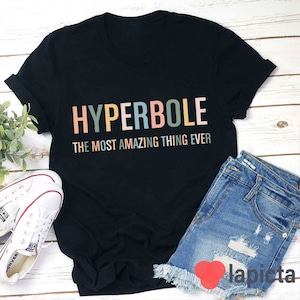 Puede incluir: Camiseta negra con el texto "HYPERBOLE THE MOST AMAZING THING EVER" en colores arcoíris.