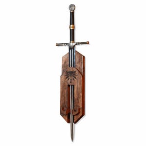 May include: A steel sword with a black grip, gold-colored accents, and a circular pommel, mounted on a vertical wooden plaque. The plaque features a dark wood finish and a carved wolf head emblem centered above the blade's resting position.