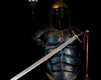 May include: A silver sword with a gold hilt and crossguard is displayed against a backdrop of a dark green and brown metal armor suit. The armor is worn by a mannequin and has a gold helmet with a chainmail coif.