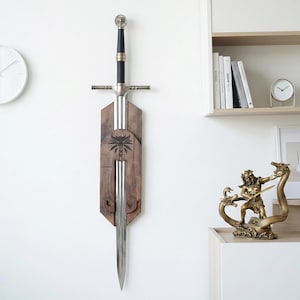 May include: A silver-toned metal sword with a black grip and a wolf-head pommel, mounted vertically on a dark brown wooden wall plaque. The plaque features a laser-engraved wolf head emblem centered above the blade, which tapers to a sharp point.