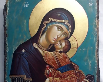 May include: A religious icon depicting the Virgin Mary holding the baby Jesus. The icon is painted on a wooden panel with a blue background and gold accents. The Virgin Mary is wearing a blue robe and a gold crown. The baby Jesus is wearing a white robe and a gold halo. The icon is inscribed with the Greek letters "MP, OY, IC XC".