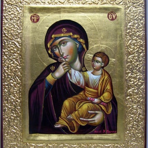 Può includere: Un'icona religiosa che raffigura la Vergine Maria che tiene in braccio il bambino Gesù. L'icona è dipinta in uno stile tradizionale con accenti in foglia d'oro e l'iscrizione "MP OY" in alto. L'iscrizione "XEIP X ПАНNA" è in basso.