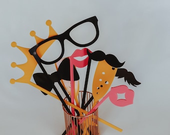 May include: A set of colorful party props, including a crown, a mustache, lips, and glasses, are arranged in a copper wire holder.