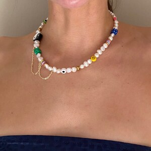 May include: A white pearl necklace with colorful beads, including green, blue, yellow, and black. The necklace features a charm with a yin yang symbol and a gold chain.
