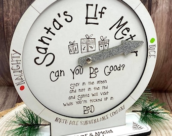Op de afbeelding: Een witte houten kerst-elfenmeter met een zilveren pijlwijzer. De meter heeft een rode, gele en groene kleurschaal met de woorden "Naughty", "Danger Zone" en "Nice". De meter heeft ook de tekst "Santa's Elf Meter", "Can You Be Good?" en "North Pole Surveillance Company". De meter is gepersonaliseerd met de namen "Oliver & Amelia".