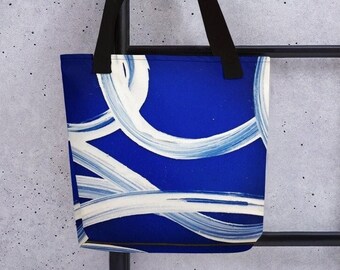 Puede incluir: Una bolsa de tela azul con pinceladas abstractas blancas. La bolsa tiene asas negras.