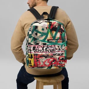 May include: A black backpack with a colourful, abstract design featuring graffiti-style lettering and images. The design includes the words "Opening Fall" and "coolenchenow".