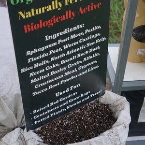 K&ouml;nnte beinhalten: Ein Sack mit organischer Blumenerde und einem Schild. Auf dem Schild steht "Organische Blumenerde, nat&uuml;rlich ged&uuml;ngt, biologisch aktiv". Zutaten: Torfmoos, Wurmkot usw. F&uuml;r Hochbeete und Topfpflanzen.