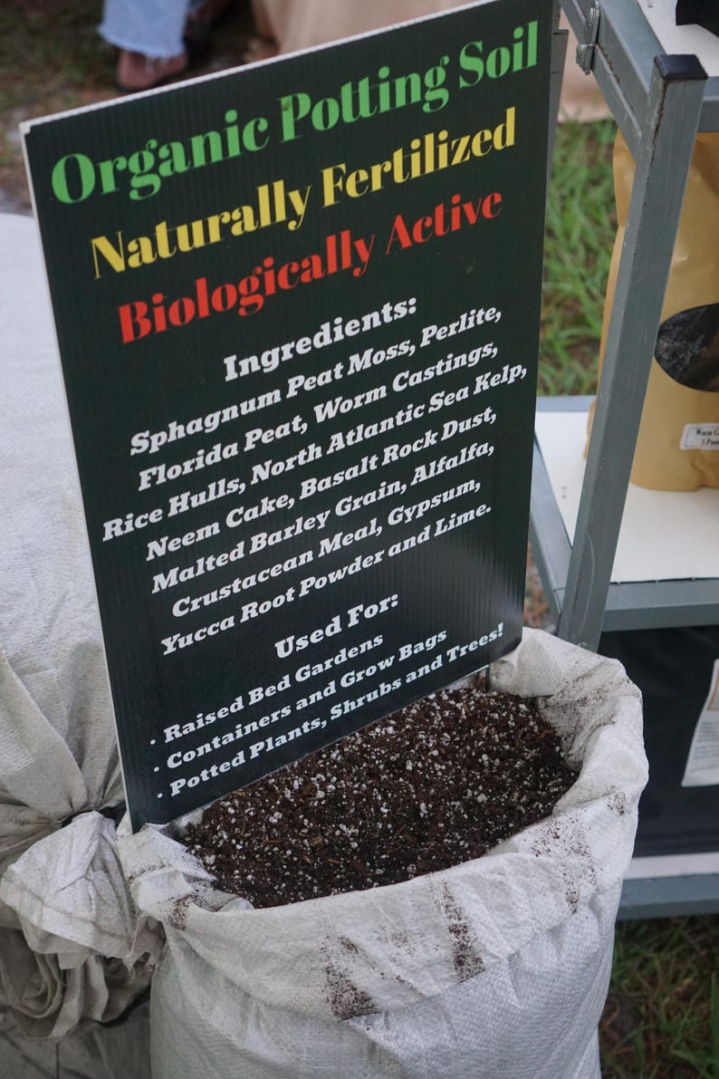 K&ouml;nnte beinhalten: Ein Sack mit organischer Blumenerde und einem Schild. Auf dem Schild steht "Organische Blumenerde, nat&uuml;rlich ged&uuml;ngt, biologisch aktiv". Zutaten: Torfmoos, Wurmkot usw. F&uuml;r Hochbeete und Topfpflanzen.