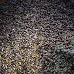 K&ouml;nnte beinhalten: Nahaufnahme einer Mischung aus organischen Gartenbaumaterialien. Das Bild zeigt eine Vielzahl von Texturen und Farben, darunter dunkelbraune Pellets, hellbraune Granulate und graue, pulverf&ouml;rmige Erde. Die Materialien werden wahrscheinlich zur Bodenverbesserung verwendet.