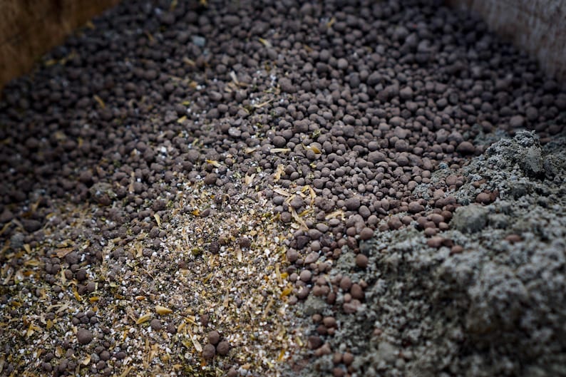 K&ouml;nnte beinhalten: Nahaufnahme einer Mischung aus organischen Gartenbaumaterialien. Das Bild zeigt eine Vielzahl von Texturen und Farben, darunter dunkelbraune Pellets, hellbraune Granulate und graue, pulverf&ouml;rmige Erde. Die Materialien werden wahrscheinlich zur Bodenverbesserung verwendet.