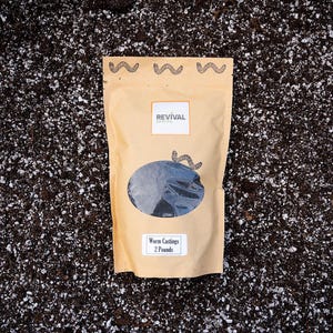 Two pounds of worm castings in a brown resealable pouch bag that is laid upon a potting soil background.