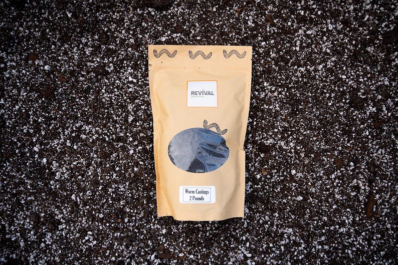 Two pounds of worm castings in a brown resealable pouch bag that is laid upon a potting soil background.