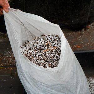 K&ouml;nnte beinhalten: Ein wei&szlig;er Plastiksack gef&uuml;llt mit Blumenerde. Die Mischung ist eine Kombination aus dunkelbrauner Erde, wei&szlig;em Perlit und kleinen Holzst&uuml;cken. Der Sack ist ge&ouml;ffnet und gibt den Inhalt frei.