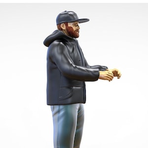 May include: A man wearing a black hooded jacket and a black baseball cap. He has a red beard and is standing with his arms outstretched.
