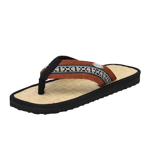 Könnte beinhalten: Braune Flip-Flops mit geflochtenem Strohhufbett und schwarzer Sohle. Der Riemen hat ein blaues und weißes geometrisches Muster und das Wort "CONNEY" ist auf den Riemen gedruckt.