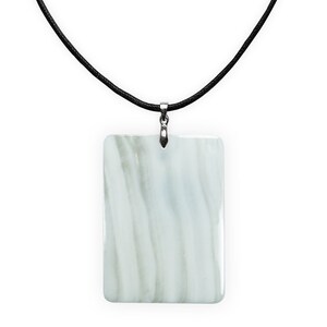 Puede incluir: Un colgante blanco con un patrón de mármol cuelga de un collar de cordón negro.
