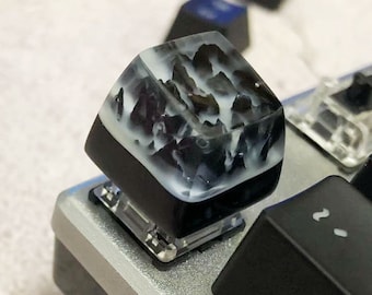 May include: A black and white resin keycap with a cloudy, marbled design. The keycap is mounted on a black keyboard.