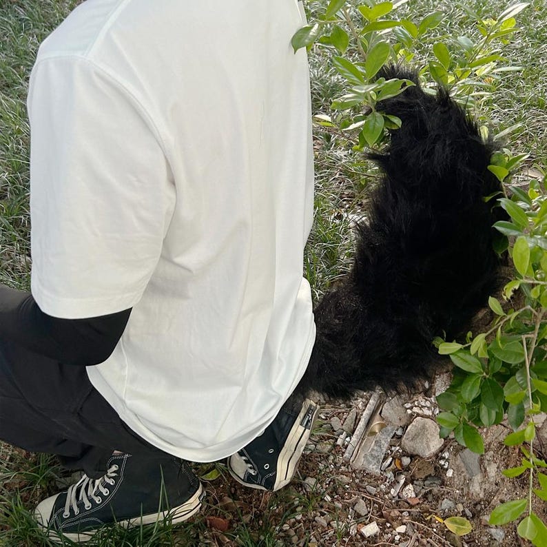 May include: A person wearing a white t-shirt and black pants with a black furry tail attached to their waist.