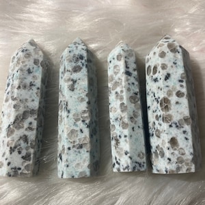Pode incluir: Quatro obeliscos de cristal salpicados em azul claro e branco. Cada obelisco tem um topo pontiagudo e uma base retangular. Os cristais têm um padrão salpicado de cinza e preto.
