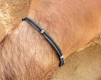 May include: A silver bracelet with a braided design and small silver beads. The bracelet is worn on a person's wrist.
