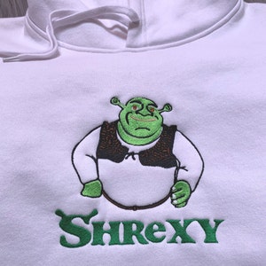 May include: White hoodie featuring an embroidered green image of Shrek wearing a brown vest and the text "Shrexy" in green underneath.