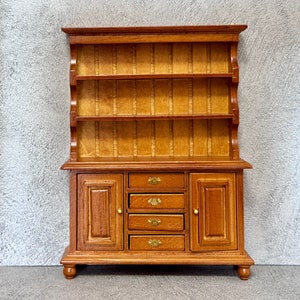 Op de afbeelding: Een houten dressoir met een bovenste plank en een onderste kast met vier lades en twee deuren. Het dressoir is lichtbruin van kleur met messing beslag.