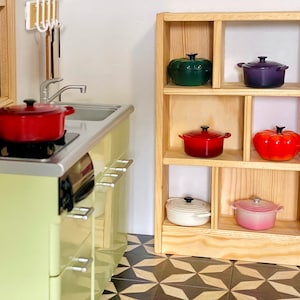 May include: A wooden shelf unit with six shelves, each holding a different colored cast iron pot. The pots are red, green, white, pink, orange, and purple.