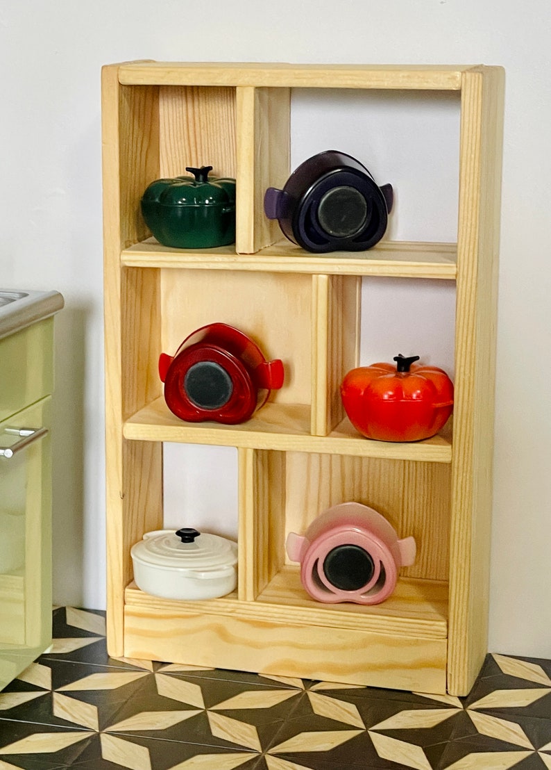 May include: A wooden shelf unit with six compartments, each holding a different colored ceramic pot with a lid. The pots are in shades of green, purple, red, pink, and white.