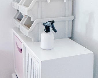 May include: White plastic storage bins with a white spray bottle on top. The bins are stacked on top of each other and have a pink and white storage unit underneath.