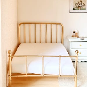 May include: A gold metal bed frame with a white mattress. The bed frame has a simple design with vertical bars and a horizontal bar at the foot of the bed.