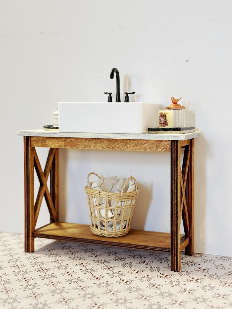 May include: A white porcelain sink with a black faucet sits on a wooden vanity with a woven basket on the lower shelf. The vanity has a rustic, farmhouse style with a distressed wood finish.