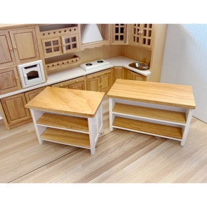 Puede incluir: Dos islas de cocina en miniatura de madera y blanco con dos estantes cada una. Las islas son de madera con un acabado pintado en blanco y una tapa de madera natural.
