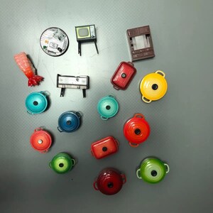 May include: A collection of miniature kitchen and home decor items, including a stove, a television, a cabinet, a table, and a variety of colourful pots and pans.