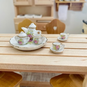 以下が含まれることがあります： 木製のテーブルの上に置かれた、花柄のミニチュア磁器製ティーセット。セットには、ティーポット、クリーマー、シュガーボウル、ティーカップとソーサーが2つ含まれています。