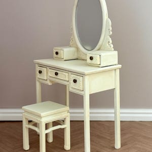 May include: A cream-coloured vanity set with an oval mirror, two small drawers, and three larger drawers. The set includes a matching stool. The vanity has ornate detailing and a vintage aesthetic.