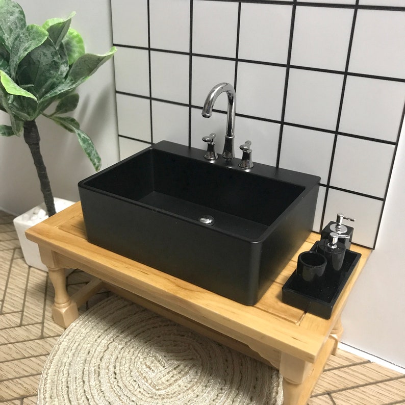 May include: A black porcelain sink with a chrome faucet and three handles sits on a wooden countertop. A small wooden tray with two black soap dispensers and a black tumbler sits on the countertop.