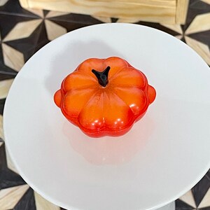 May include: Orange pumpkin-shaped ceramic casserole dish with a black knob on the lid.