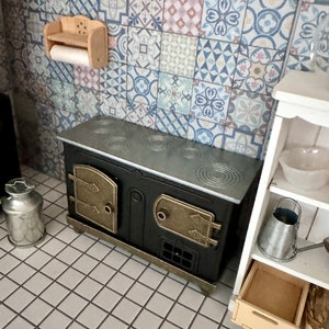 May include: A miniature black and gold stove with a silver top, a wooden paper towel holder, a metal milk can, and a white shelving unit containing a bowl, a metal watering can, and a wooden crate, all set against a blue and white patterned wall.