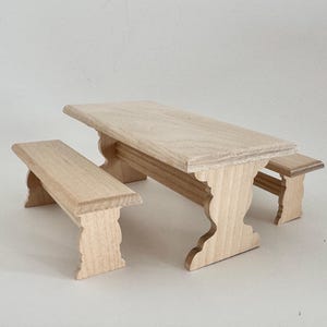 Peut inclure: Un ensemble de pique-nique miniature en bois, comprenant une table rectangulaire et deux bancs. L'ensemble est en bois clair non fini, mettant en valeur le grain naturel. La table mesure environ 15 cm de long.