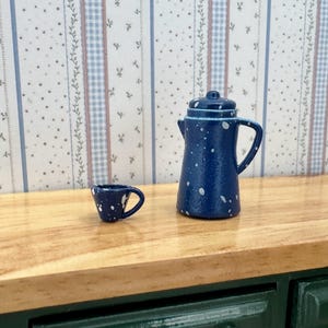 May include: A miniature dark blue coffee pot and a matching small cup, both featuring a white speckled pattern. The coffee pot has a lid, a handle, and a spout, while the tiny cup includes a small handle, designed for a dollhouse setting.