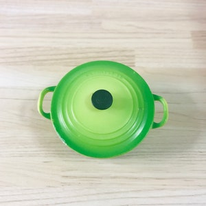 May include: A green enamelled cast iron pot with a black knob on the lid. The pot has two handles.